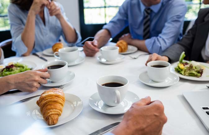 Profesionales reunidos alrededor de una mesa con cafe y desayuno para representar las soluciones de Coffitalia destinadas a empresas y oficinas locales.